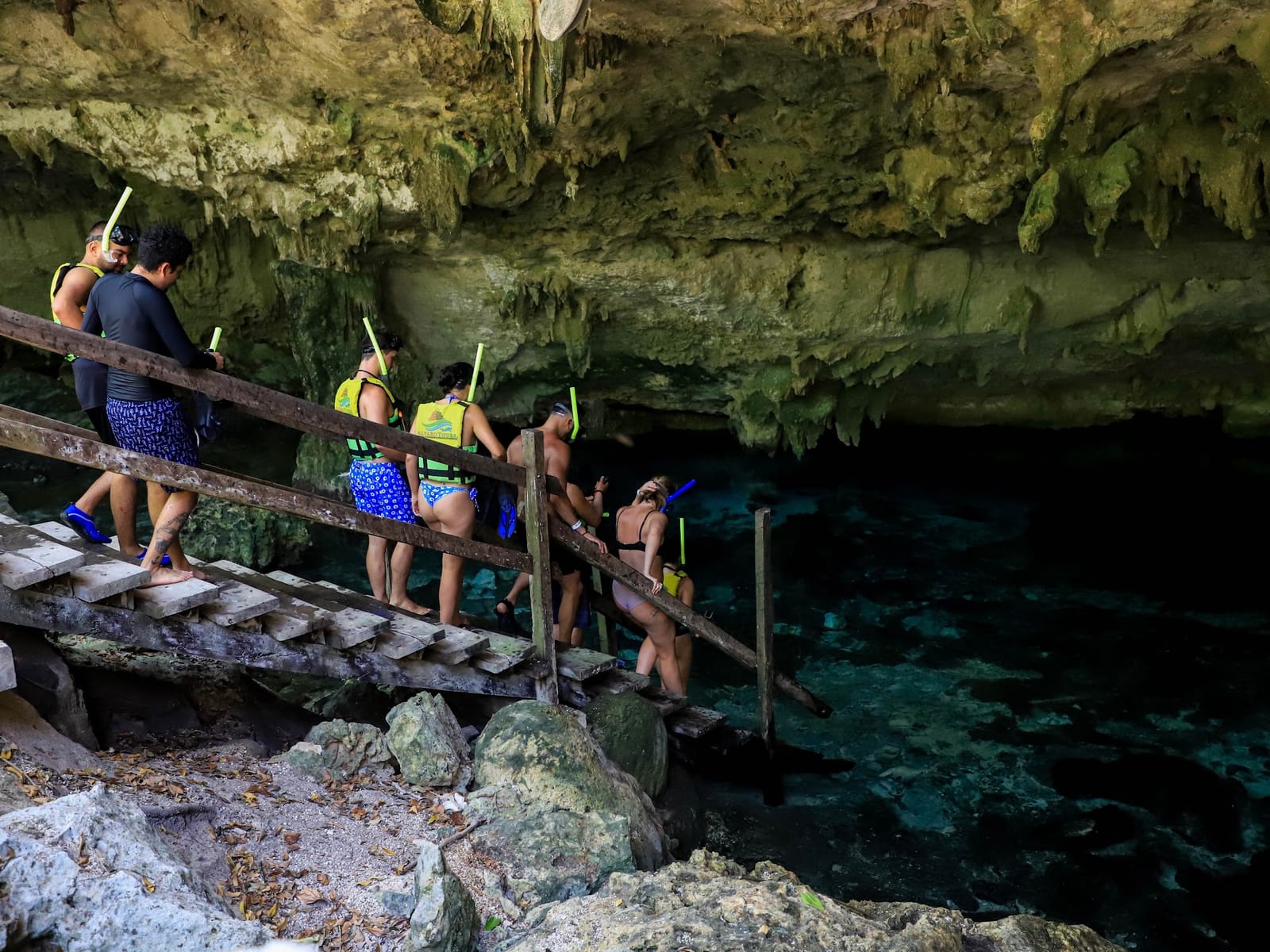 Grupo pequeño bajando por la escalera de madera hacia el agua del Cenote Dos Ojos