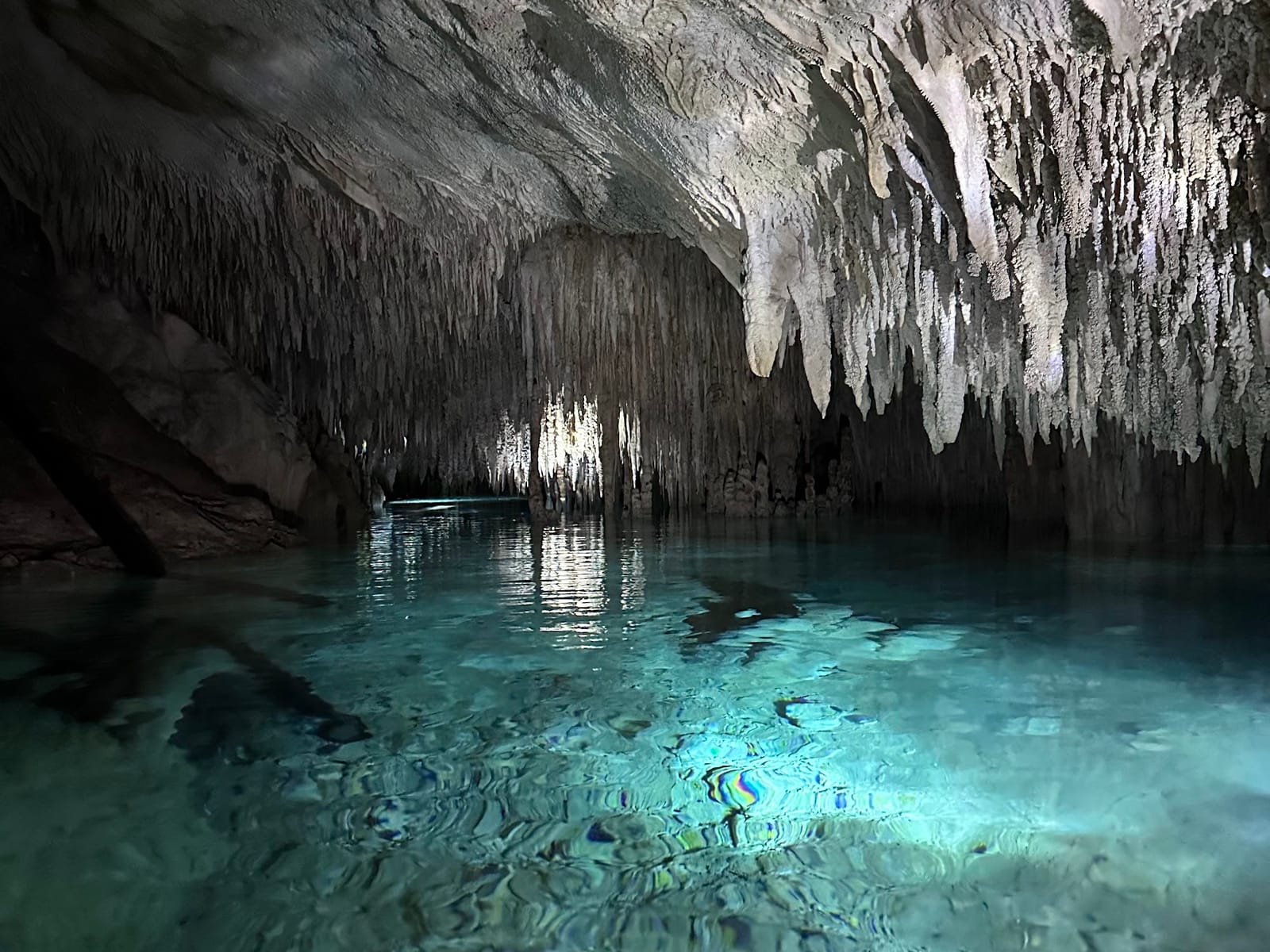 Galerie weißer Stalaktiten, die sich im türkisfarbenen Wasser eines Gangs im Cenote Los Monos spiegeln