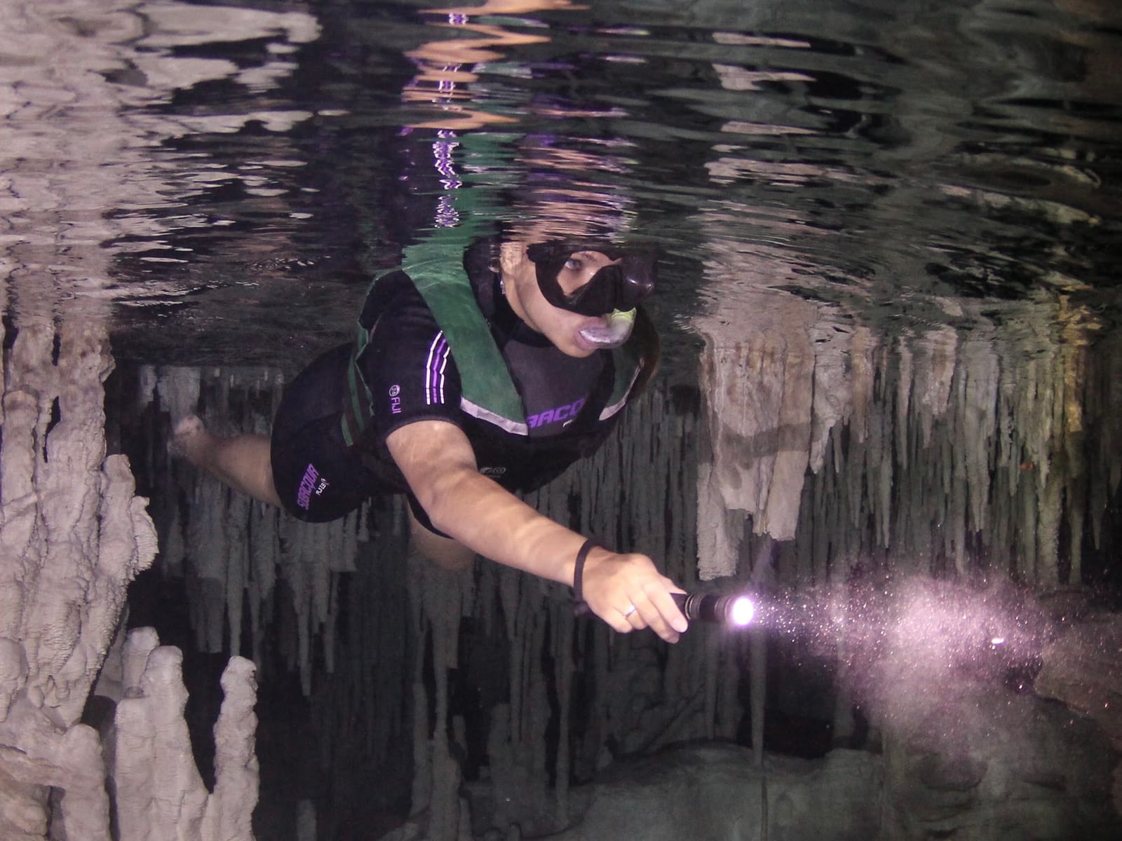 Schnorchlerin mit Weste beleuchtet versunkene Tropfsteine mit ihrer Tauchlampe, Cenote Los Monos