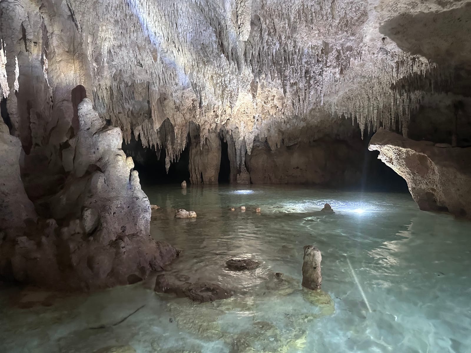 Halle voller Stalagmiten und Stalaktiten im Lampenlicht über flachem, klarem Wasser, Cenote Misterio Maya