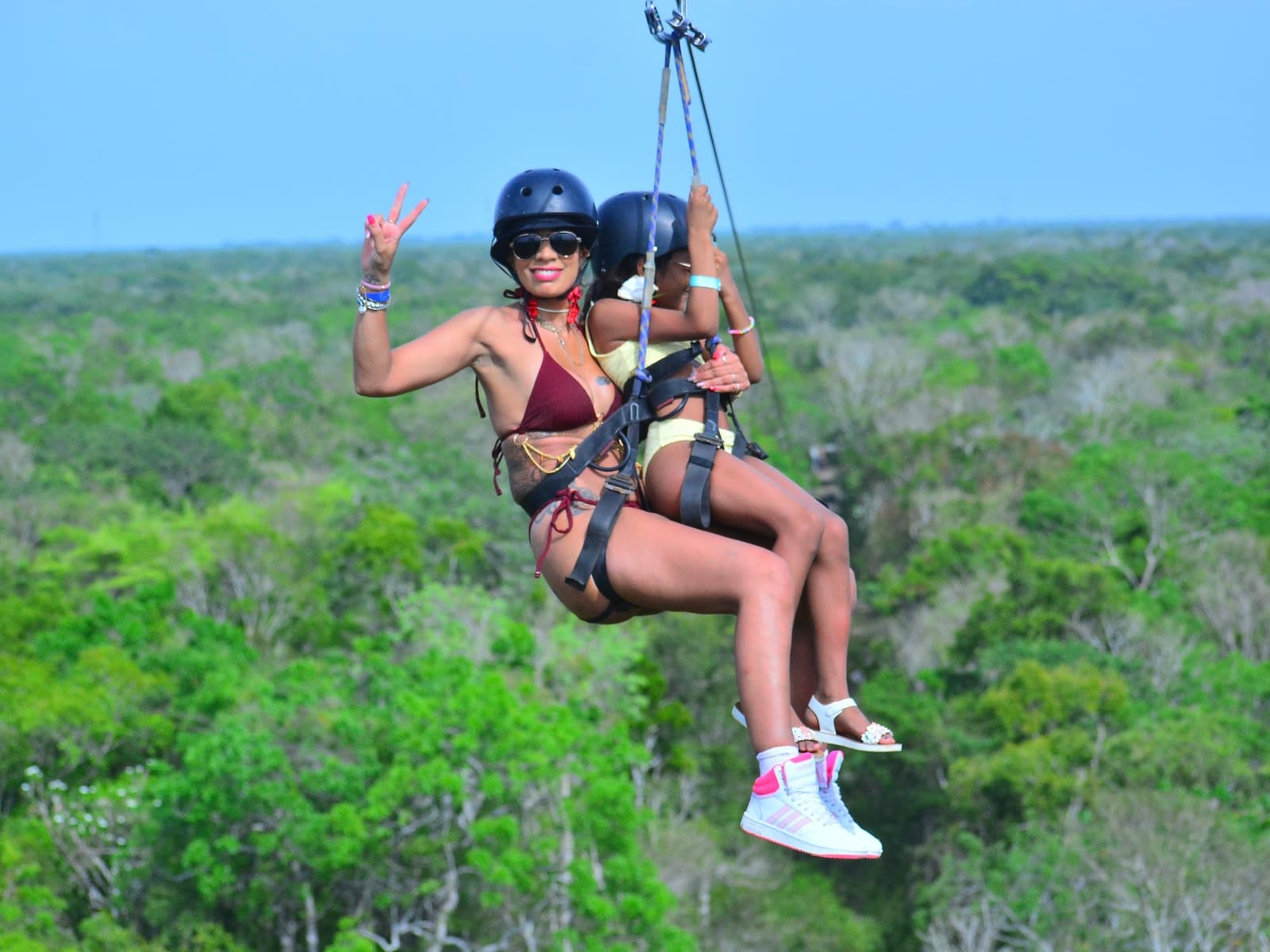 Adulta y niña en tirolesa tándem con casco y arnés sobre la selva