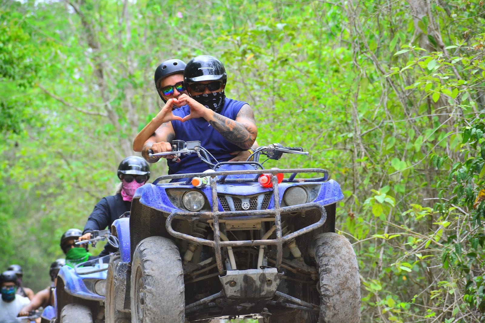 Pareja con casco hace un corazón con las manos en una cuatrimoto por la selva