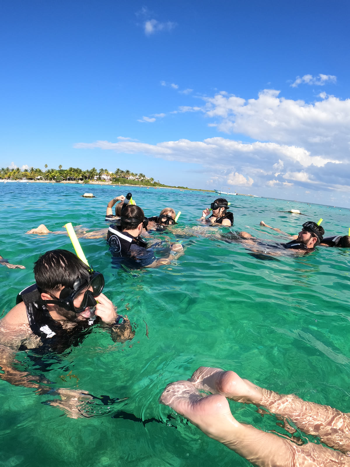 Private snorkel group in crystal-clear turquoise water at Akumal Bay — GoPro, looking up from the surface