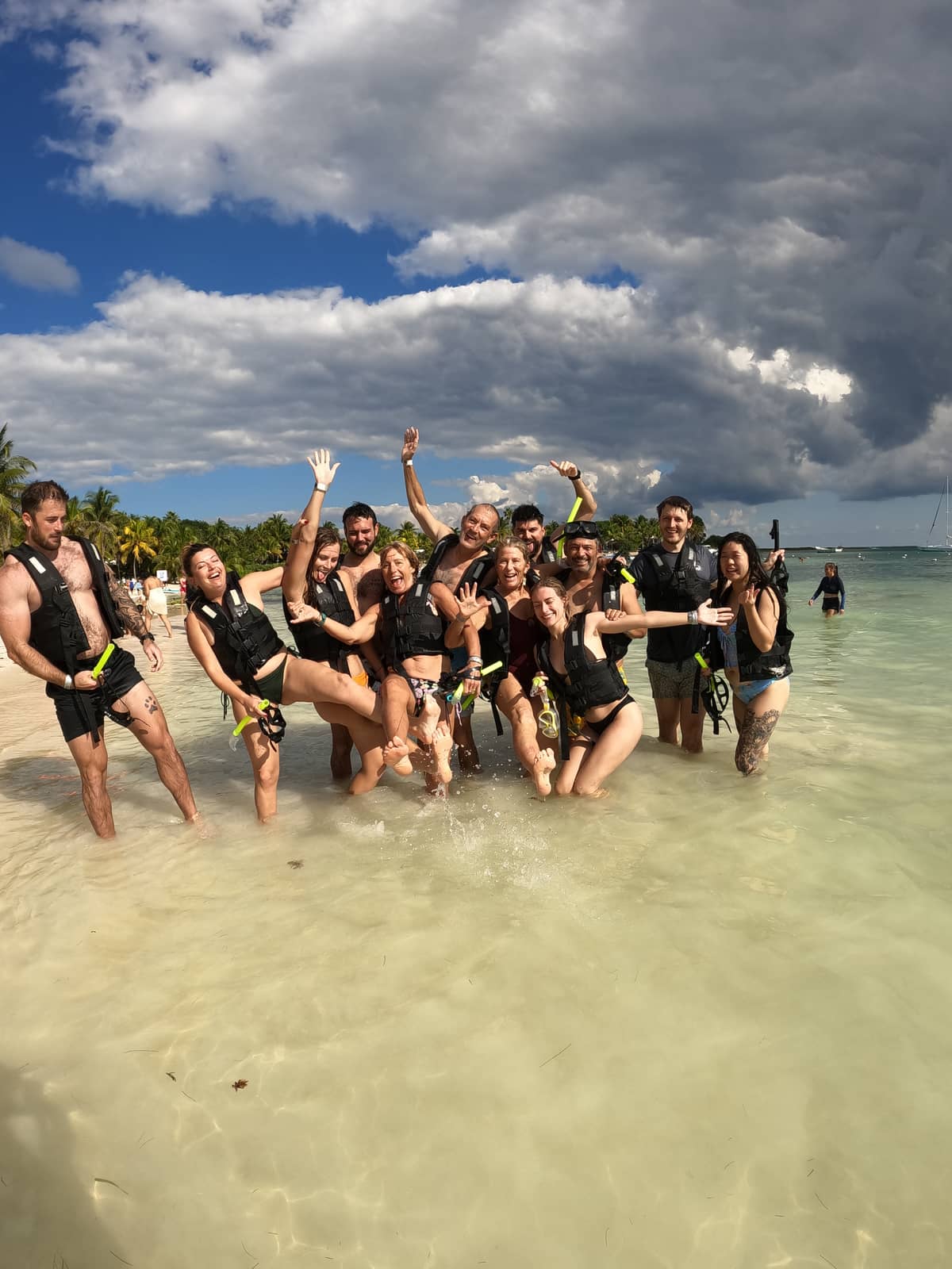 Happy snorkel tour group celebrating on Akumal Bay beach with life vests and turquoise water