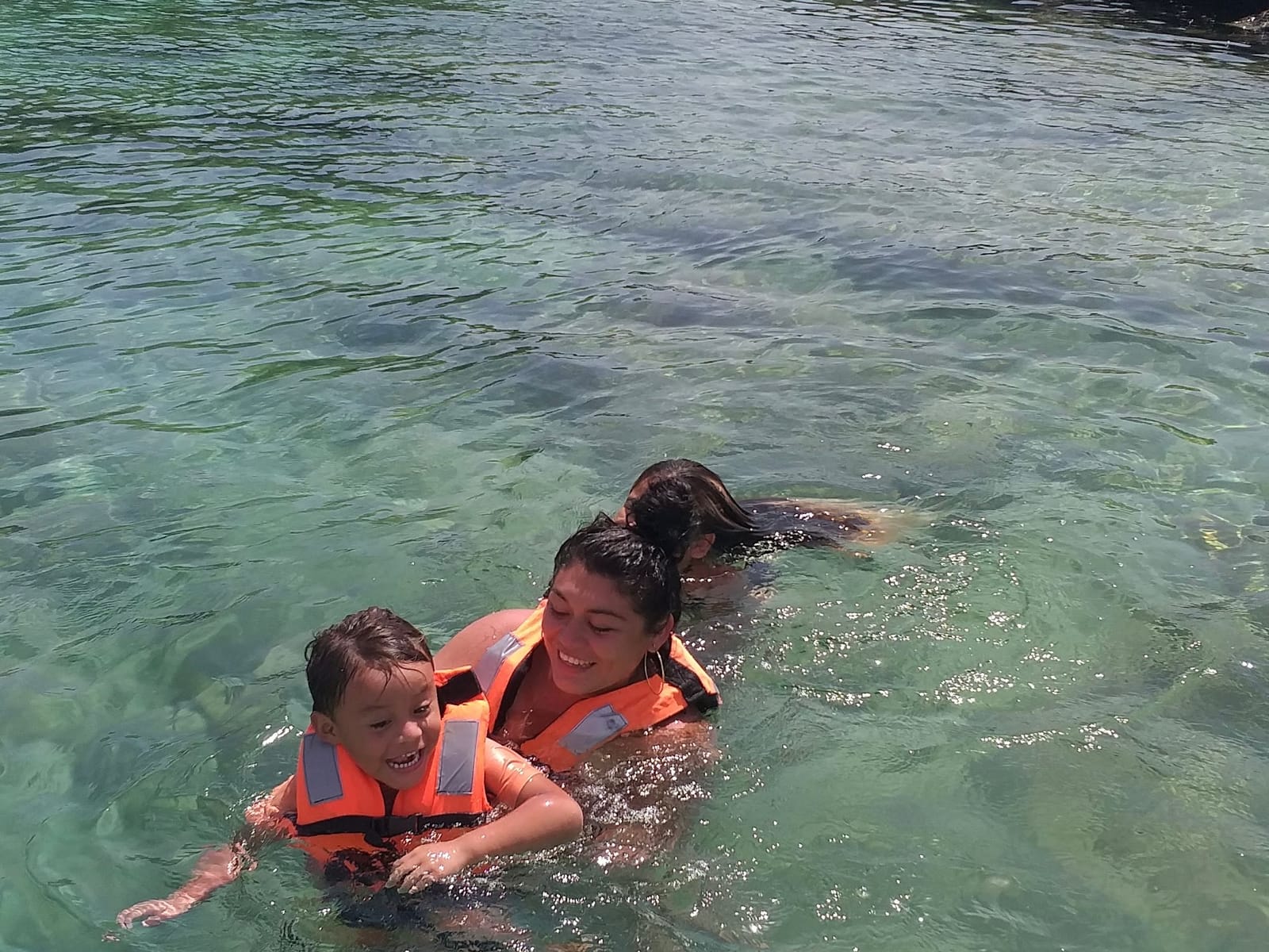 Mamá e hijo con chaleco salvavidas sonriendo en el agua clara de la laguna