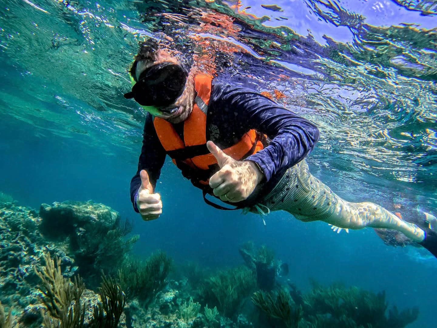 Snorkelista con chaleco salvavidas y playera UV levantando los pulgares sobre el arrecife