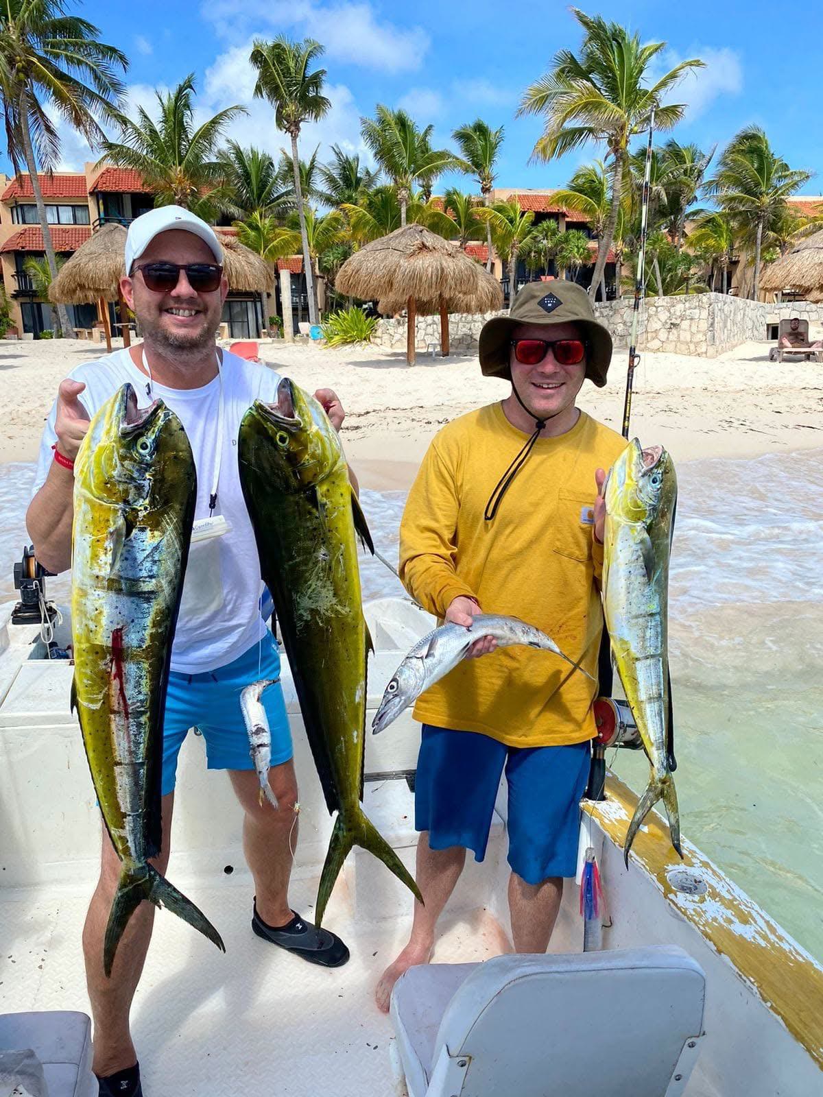 Two happy guests holding mahi-mahi and barracuda after a private fishing charter in Akumal