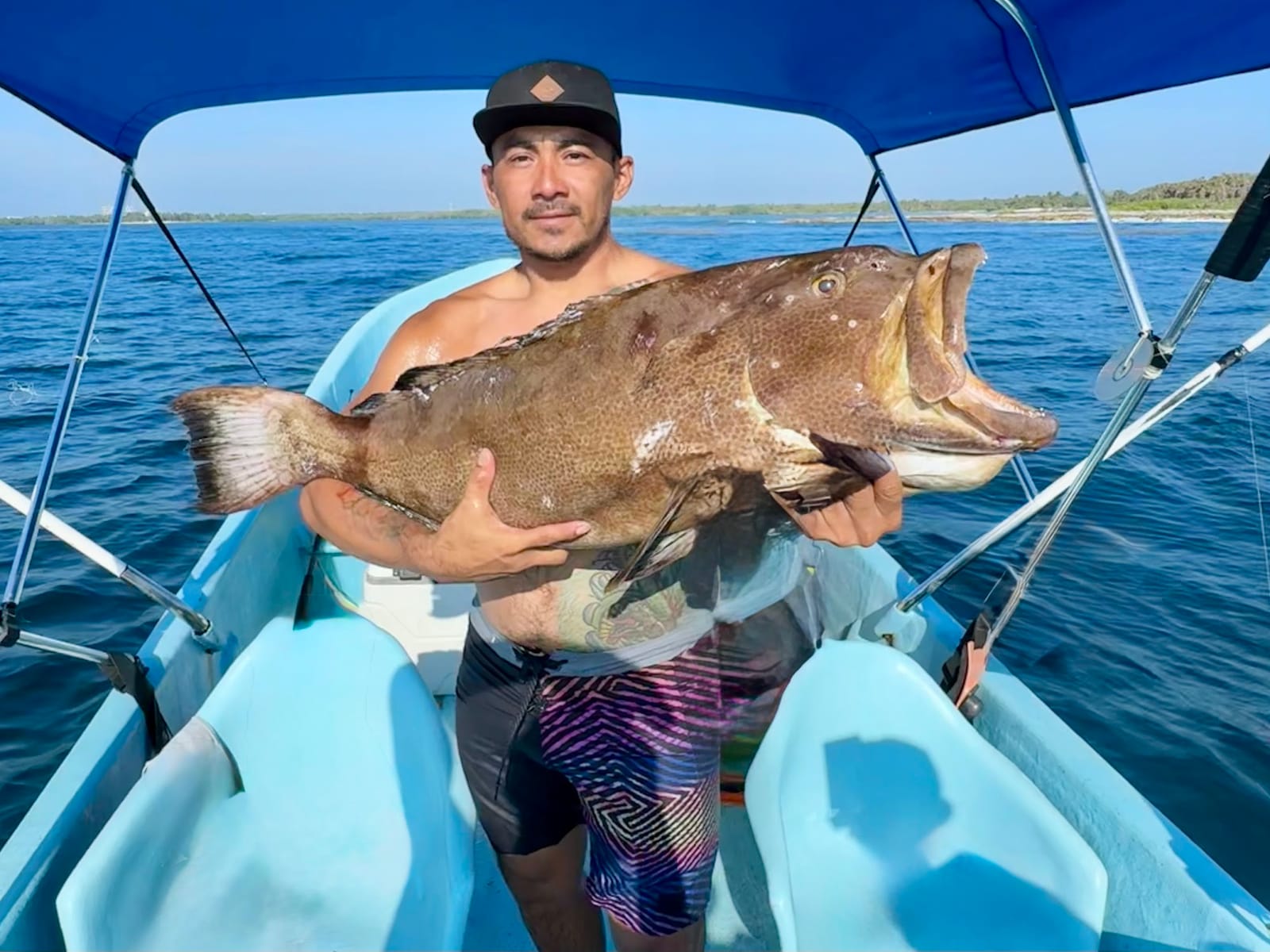 Pescador con un mero grande bajo el toldo de la lancha