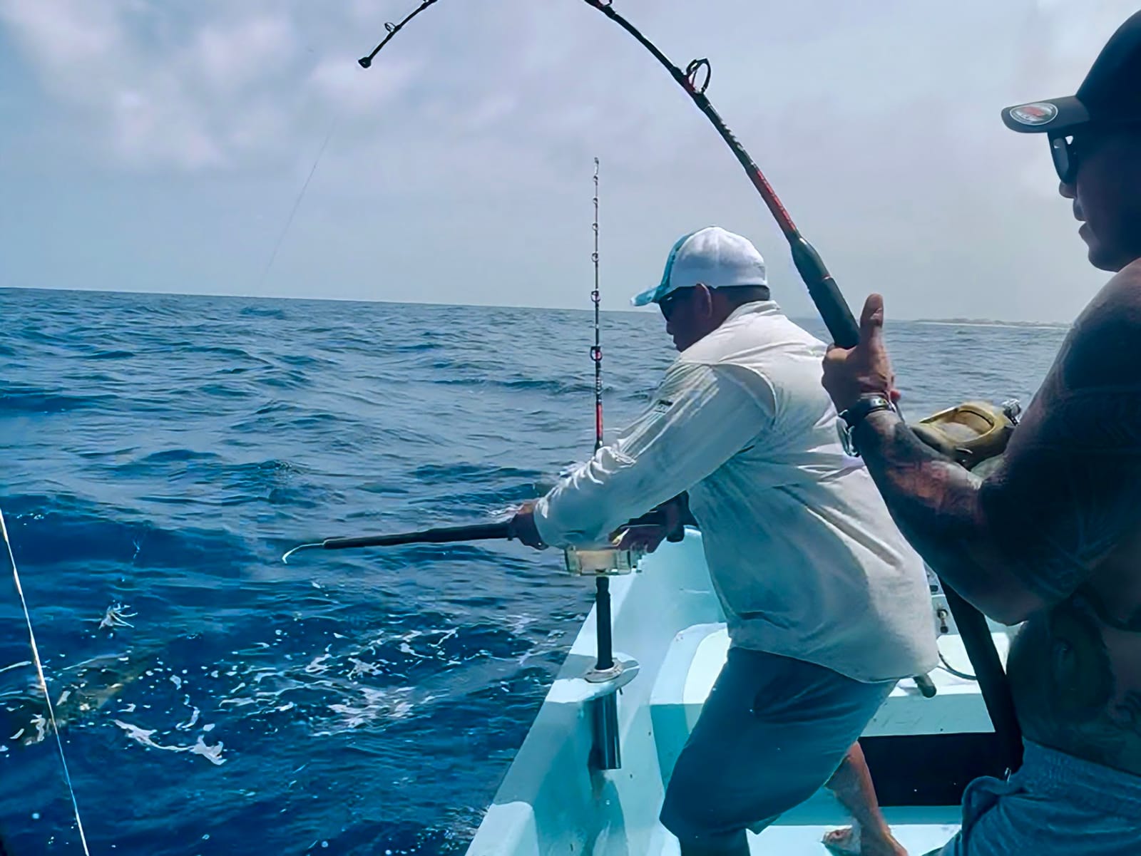 Pesca al troleo: la caña se dobla con la picada mientras el marinero acerca el pez a la lancha