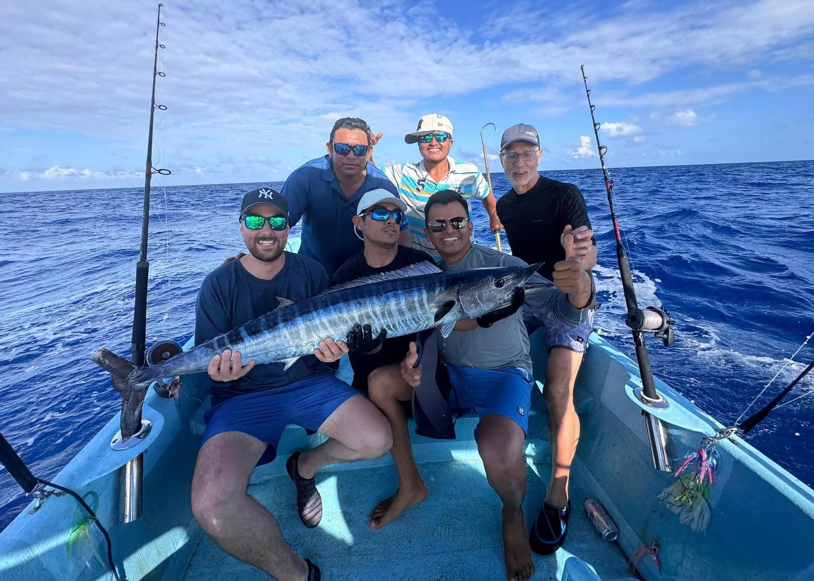 Grupo pequeño y tripulación con un wahoo a bordo, con el mar abierto detrás
