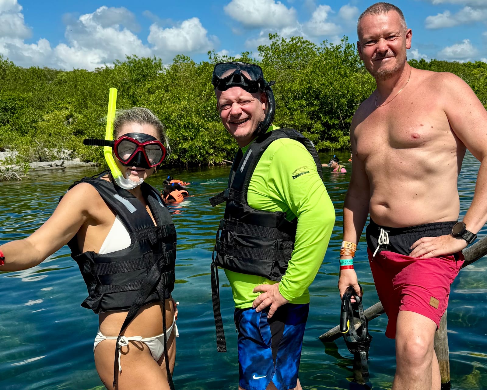 Tres visitantes con equipo de snorkel en el agua clara de la Laguna Yal-Kú, con manglares al fondo
